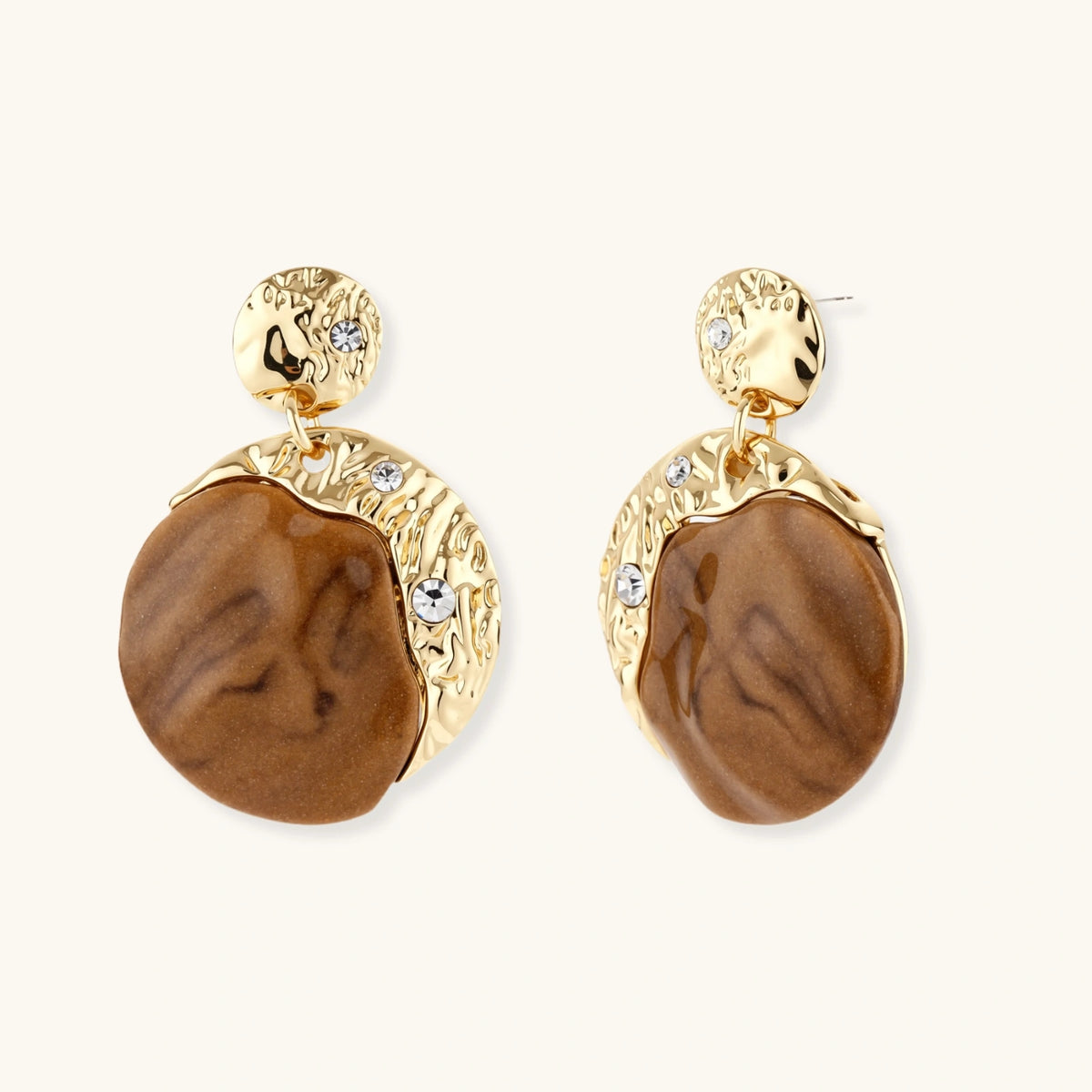 Gold-toned dangle earrings with organic brown resin stones and crystal accents on white background