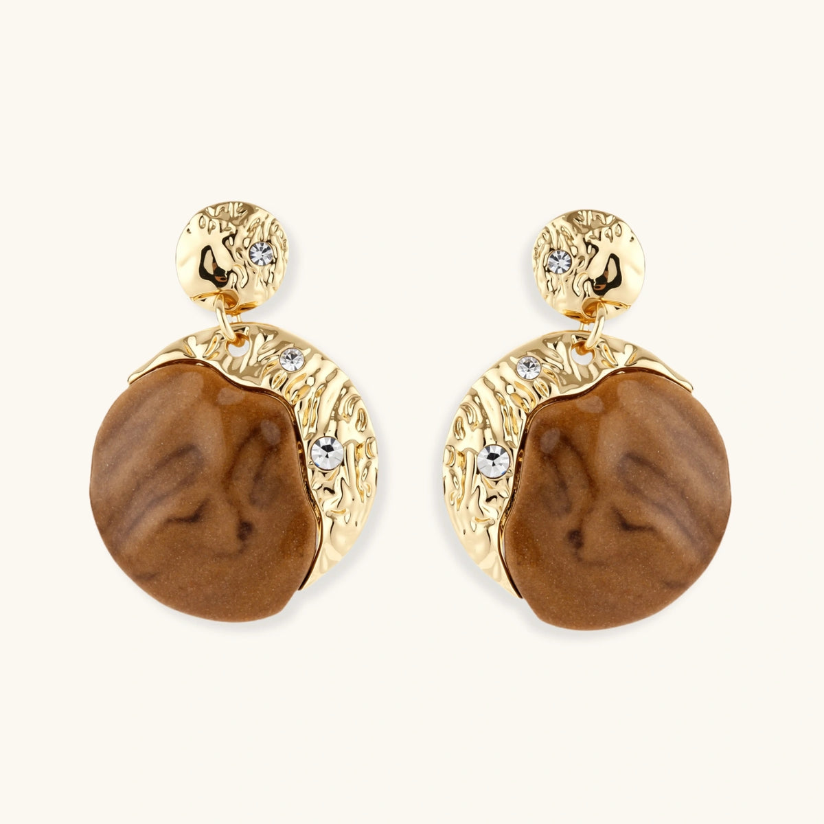 Gold-toned dangle earrings with organic brown resin stones and crystal accents on white background